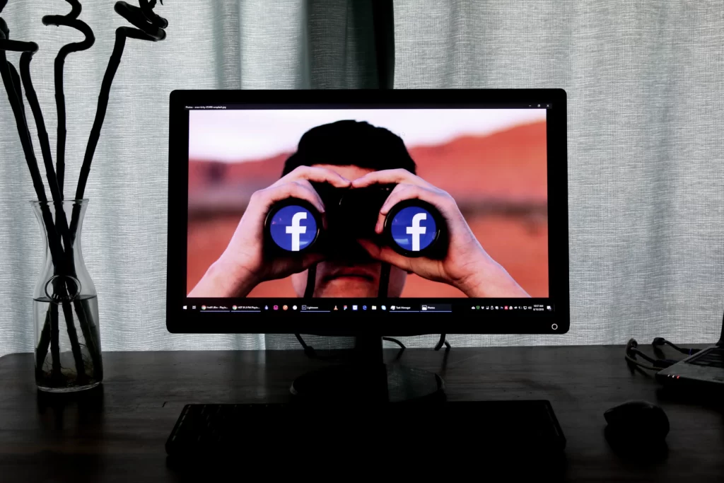 Man on television screen has binoculars that show Facebook logo. Represents a man who is watching Facebook Profile Pictures and other facebook details from his social profile.